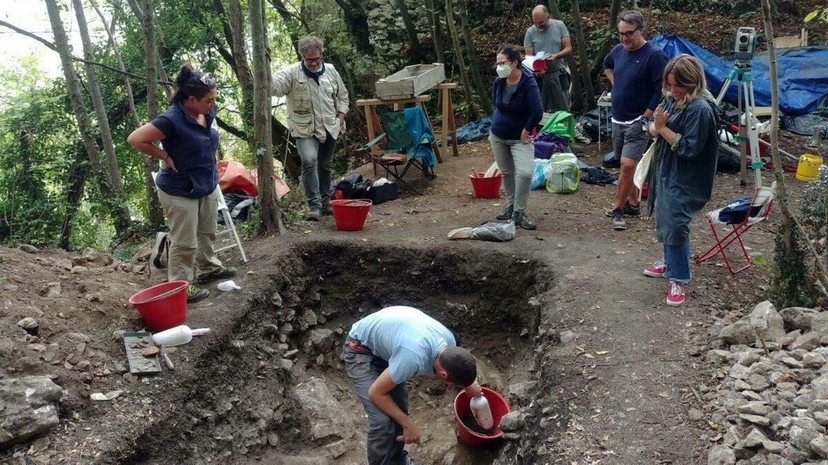 Un archeologo esamina un’area di scavo a Colombare di Villa mentre il gruppo di ricerca osserva il lavoro.