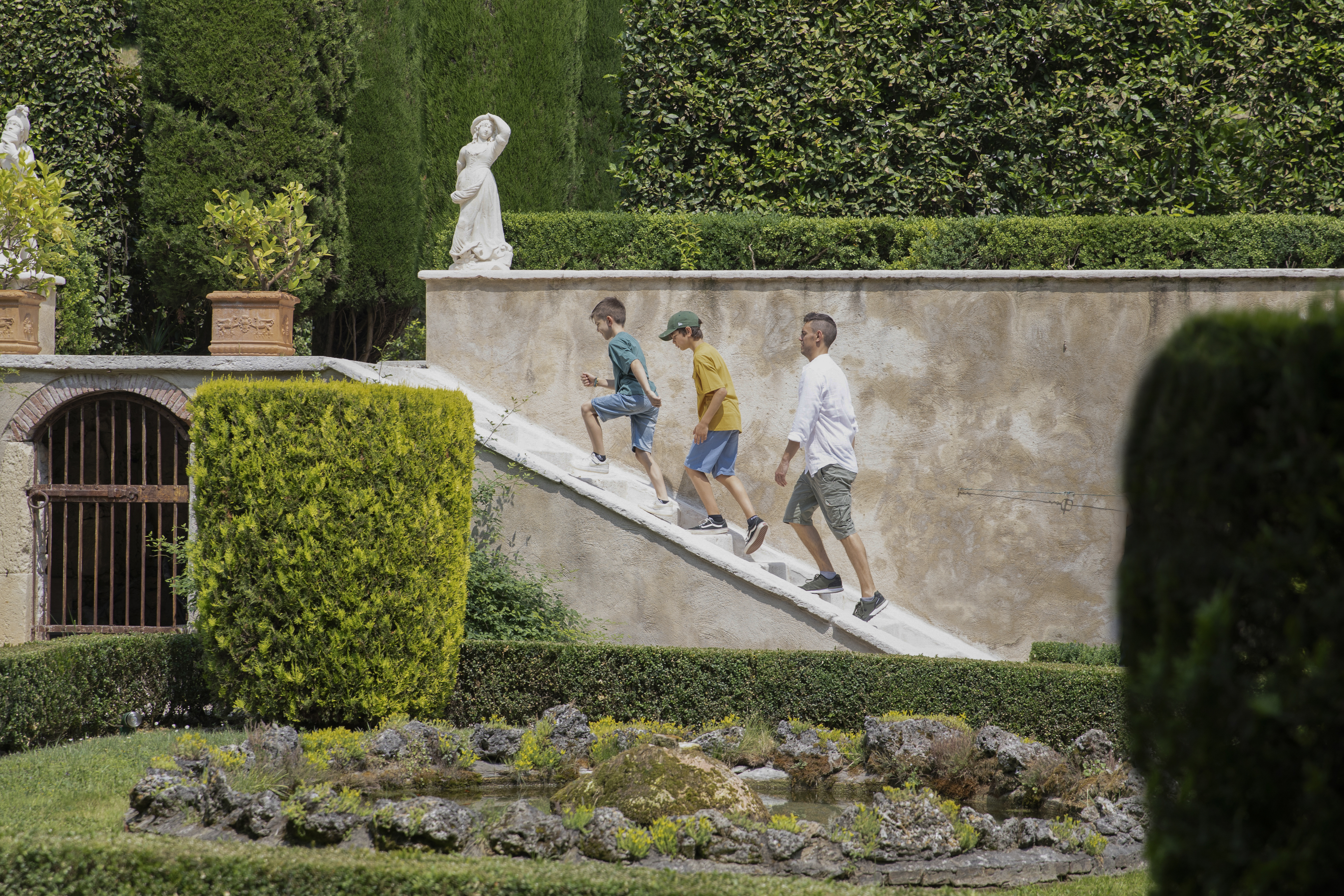 Visitatori durante una visita in autonomia al Giardino di Pojega, lungo la scalinata accanto al laghetto.